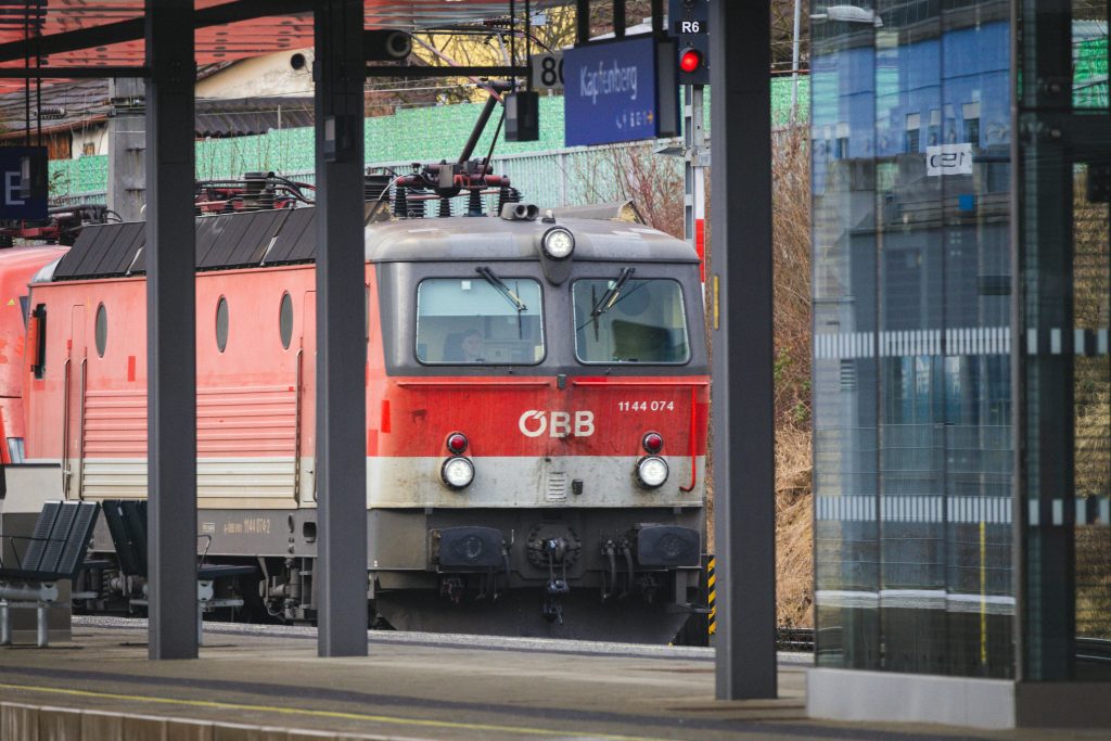 pexels-photo-19985176-19985176-1 Red ÖBB locomotive parked at a railway station platform, Austria.