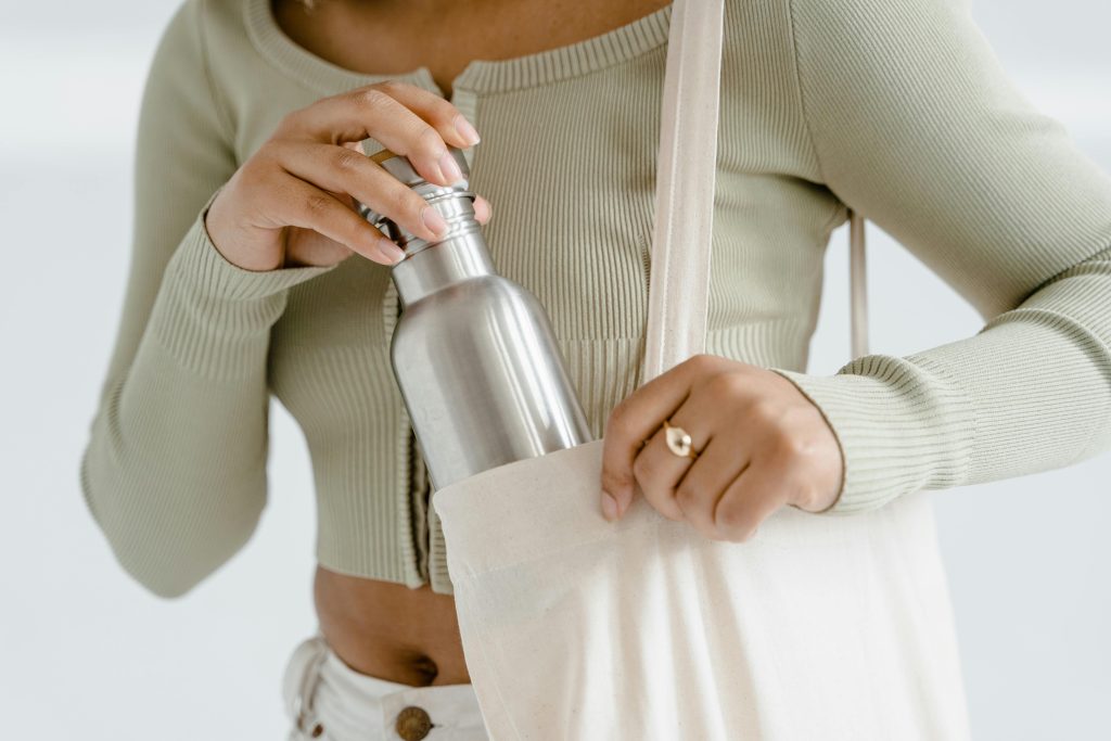 pexels-photo-7879796-7879796 Close-up of woman placing a stainless steel water bottle into a cream-colored tote bag.