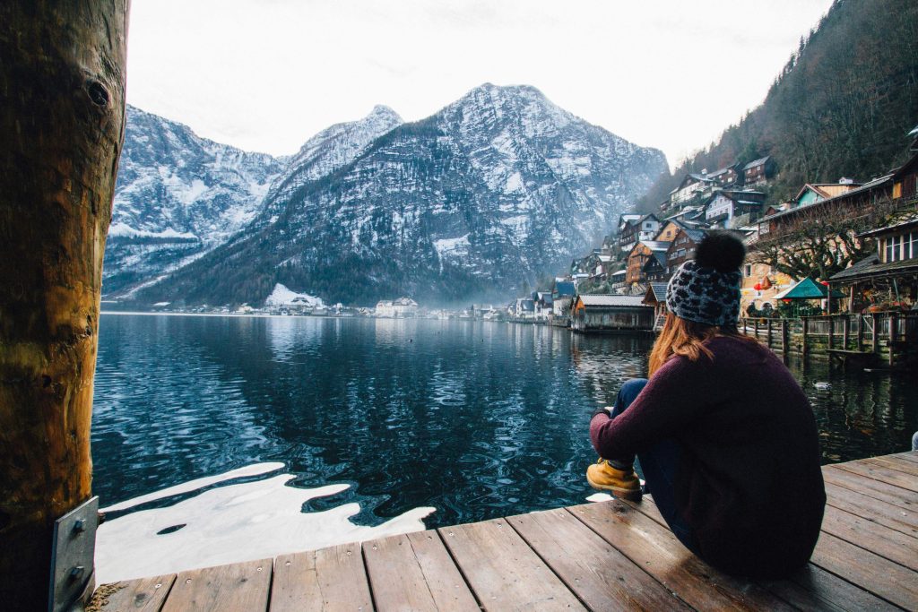 pexels-photo-789382-789382 A woman sits on a dock overlooking the serene Hallstatt Lake with snowy mountains in the background.
